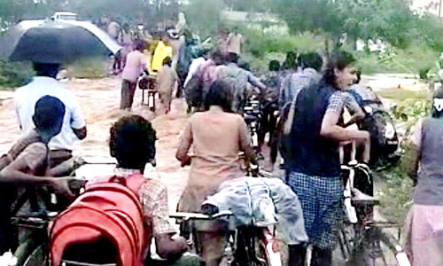 தரைப்பாலத்தில் ஓடும் மழை வெள்ளத்தில் நடந்து செல்லும் பள்ளி மாணவர்கள்