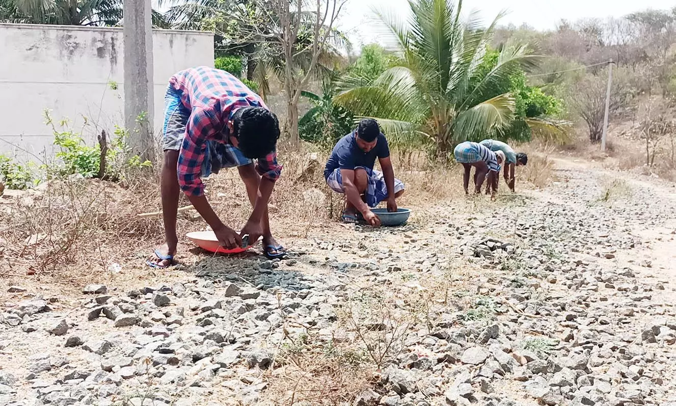 சாலையில் இருக்கும் ஜல்லியை சேகரிக்கும் பணியில் கிராம மக்கள் சாலையில் இருக்கும் ஜல்லியை சேகரிக்கும் பணியில் கிராம மக்கள்