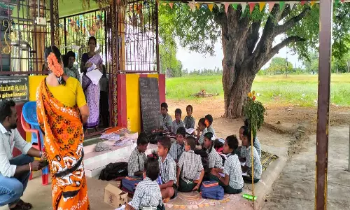 கோவில் வளாகத்தில் அமர்ந்து படிக்கும் பள்ளி மாணவர்கள்