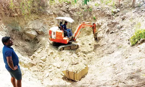 ஆட்கள் பற்றாக்குறையால் பொக்லைன் எந்திரம் மூலம் கிணறு வெட்டும் விவசாயிகள்