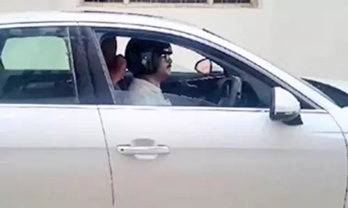 காரில் ஹெல்மெட் அணிந்து செல்லும் நபர்