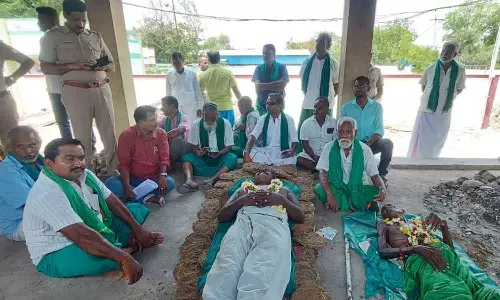 சுடுகாட்டில் பிணம் போல் படுத்து விவசாயிகள் போராட்டம்